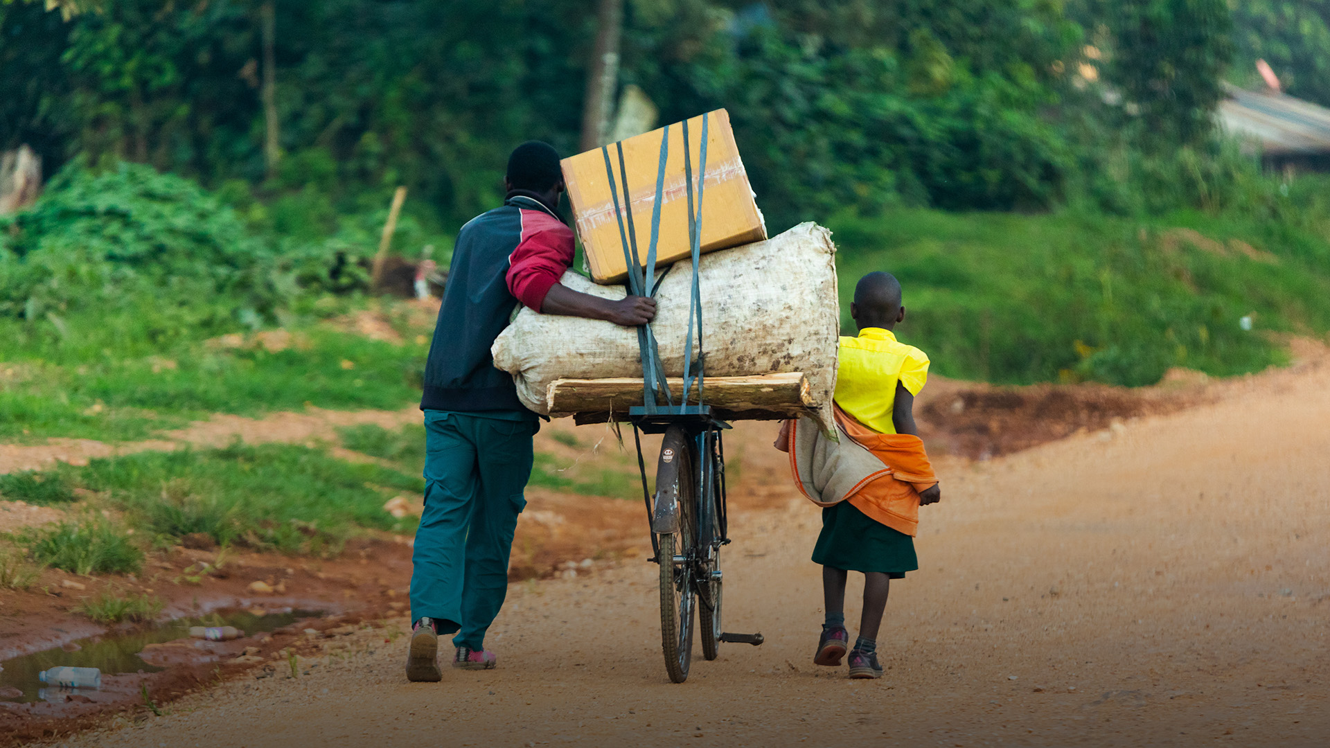 An Ugandan man and a child transporting things with a bicycle